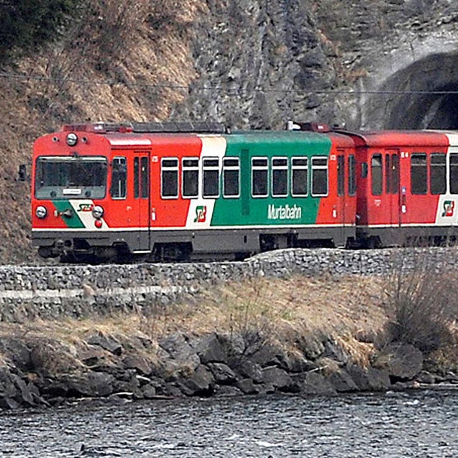Ein Bild der Murtalbahn (in alter Lackierung) mit Bergen im Hintergrund.